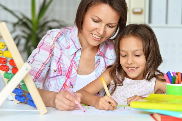 Portret ślicznej małej dziewczynki z matką rysującą razem w domu