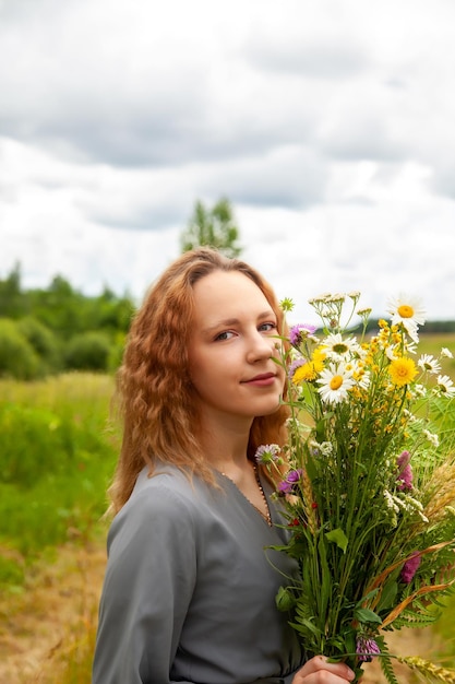 Portret ślicznej młodej dziewczyny w sukience z dzikimi kwiatami w lecie