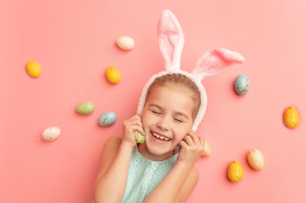 Portret ślicznej uśmiechniętej dziewczyny z uszami królika i pisanki na różowym tle