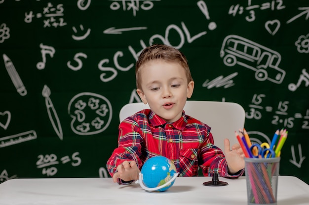 Portret śliczny chłopiec mienie w ręki małej kuli ziemskiej na blackboard tle. Gotowy do szkoły. Powrót do szkoły.