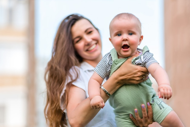 Portret słodkie dziecko patrzące prosto w kamerę na ręce mamy mama rozmazana na miejskim tle...