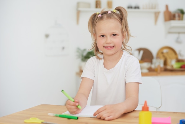 Portret Słodkie Dziewczyny Uśmiechając Się Do Kamery Podczas Odrabiania Lekcji Lub Testów W Przytulnym Wnętrzu Domu. Dziecko Uczone W Domu Podczas Koronawirusa.