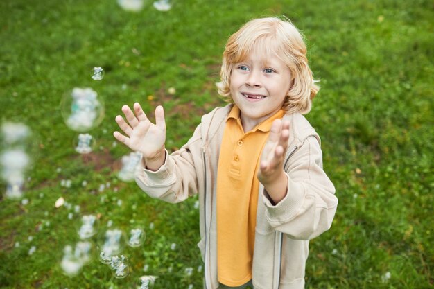 Portret Słodkiego Blond Chłopca Bawiącego Się Bąbelkami Na Zewnątrz W Parku I Uśmiechniętej Przestrzeni Kopii