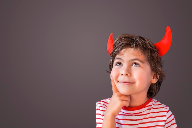Portret słodkiego chłopca noszącego rogi diabła na szarym tle