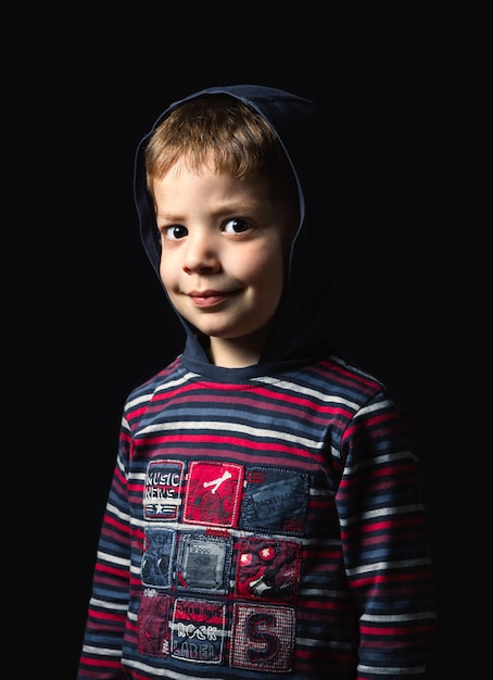 Portret słodkiego chłopca z kapturem patrząc na kamerę na czarnym tle