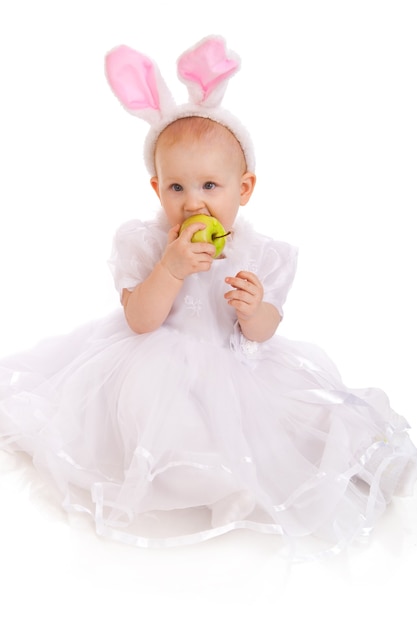 Portret słodkiego dziecka ubranego w uszy wielkanocnego królika z zielonym jabłkiem na białym tle
