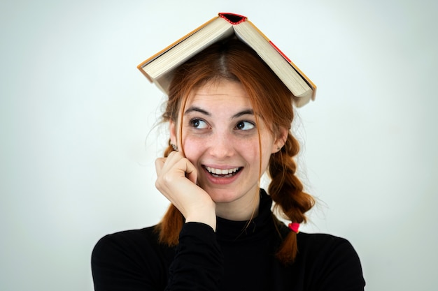 Portret śmieszna młoda uśmiechnięta studencka dziewczyna z otwartą książką na jej głowie. Koncepcja czytania i edukacji.