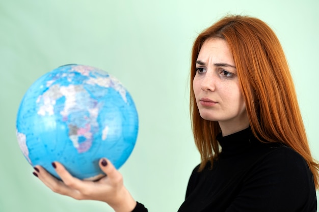 Portret smutna zmartwiona młoda kobieta trzyma geograficzną kulę ziemską świat w ona ręki. Cel podróży i koncepcja ochrony planety.