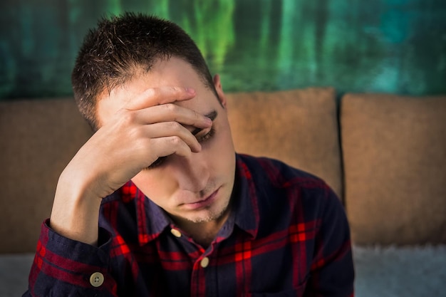 Portret smutnego zdenerwowanego młodego faceta Zamyślony mężczyzna siedzący i trzymający rękę nad głową w złym nastroju depresja ból głowy ból głowy