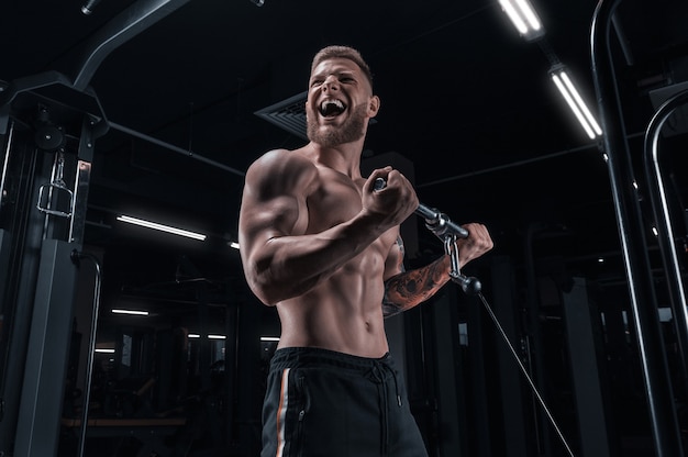 Portret sportowca pompowania bicepsów w crossoverze. Koncepcja kulturystyki i fitness. Różne środki przekazu