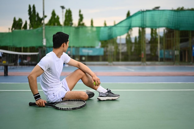 Zdjęcie portret sportowca z rakietą tenisową siedzącego na korcie tenisowym i odwracającego wzrok