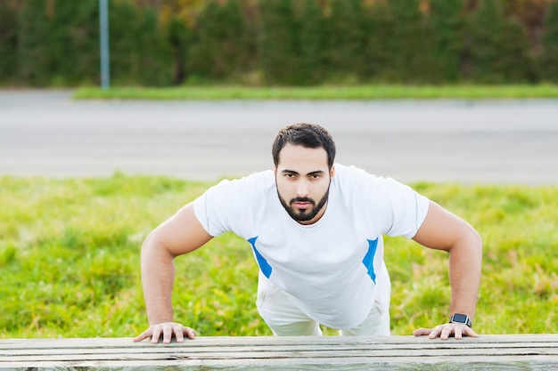 Portret sportowy mężczyzna 30s w sportowej robi pompki w zielonym parku.