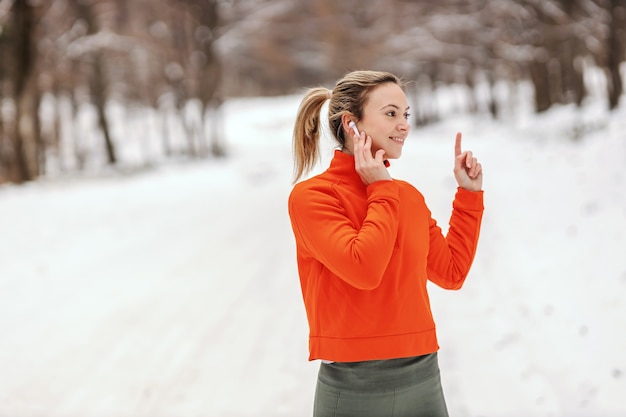 Portret sportsmenki, ciesząc się muzyką, stojąc w naturze na śnieżną pogodę. Zimowy fitness, zdrowe życie, muzyka, zabawa