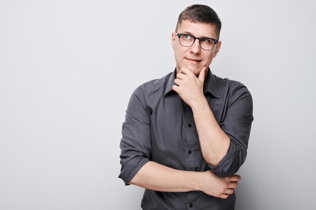 Portret sprytnego mężczyzny w koszuli dotykającego podbródka, myśli, że wątpliwości wybiera na białym tle na białym tle studia z miejsca na kopię