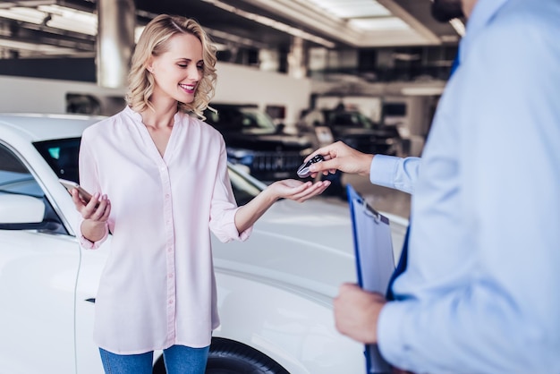 Portret sprzedawcy dającego klucze szczęśliwej kobiecie w salonie dealerskim