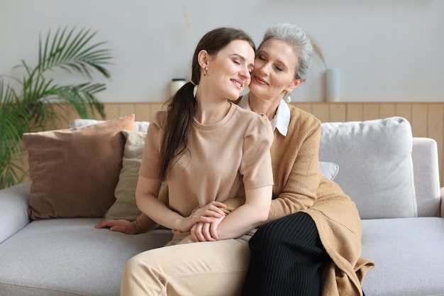 Portret starej matki i dojrzałej córki przytulanie w domu. Szczęśliwa starsza mama i dorosła córka obejmując się miłością na kanapie.