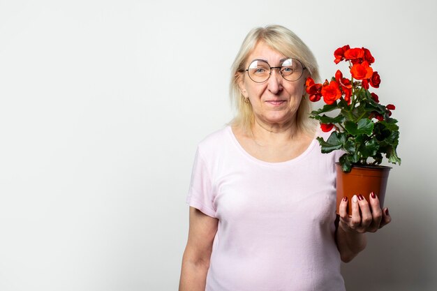 Portret Starej Przyjaznej Kobiety W Dorywczo T-shirt I Okulary Gospodarstwa Kwiat Pokoju Na Pojedyncze ściany światła. Twarz Emocjonalna. Pojęcie Pielęgnacji Roślin, Ogród Przydomowy