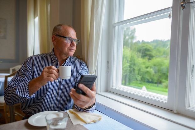 Portret starszego biznesmena picia kawy i korzystania z telefonu w domu