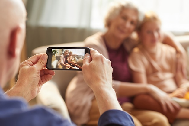 Portret starszego mężczyzny robienia zdjęcia smartfonem żony i wnuczki na rodzinne wspomnienia, skup się na ekranie smartfona