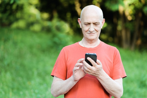 Portret starszego mężczyzny stojącego z telefonem w rękach w parku.