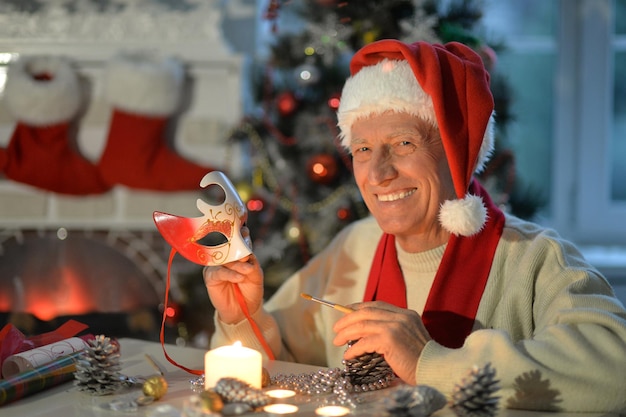 Portret starszego mężczyzny w Santa hat przygotowującym się do Bożego Narodzenia, siedzącego przy stole w domu