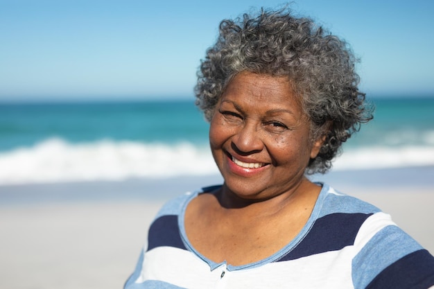 Portret starszej afroamerykańskiej kobiety stojącej na plaży z niebieskim niebem w tle, uśmiechając się do kamery