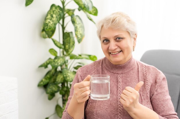 Portret starszej kobiety pije szklankę wody.