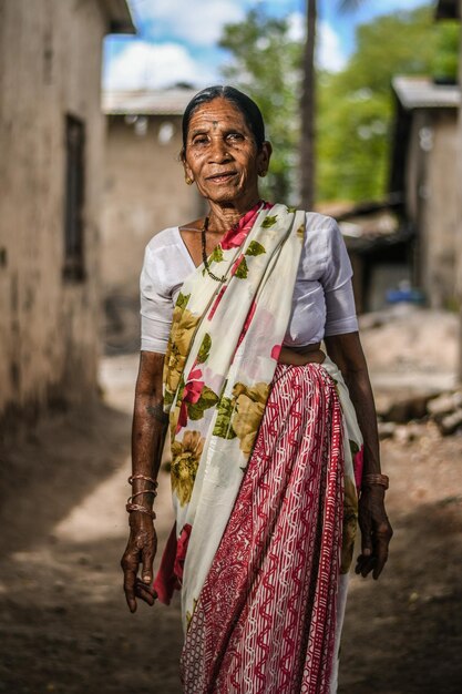 Portret starszej kobiety w sari stojącej na drodze przeciwko domom.