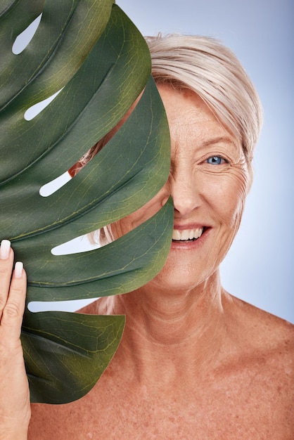 Portret starszej kobiety z liściem monstery z naturalną pielęgnacją skóry i marketingowym luksusowym spa emerytalnym w Sydney Starsza pani z pół twarzy zielonej rośliny na tle studia i zdrową dermatologią