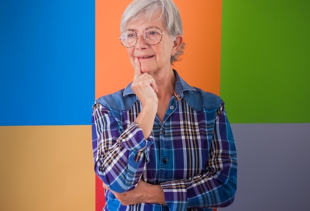 Portret starszej pięknej siwej kobiety w sportowej koszuli i okularach na białym tle nad kolorowym tłem, odwracając wzrok zamyślony