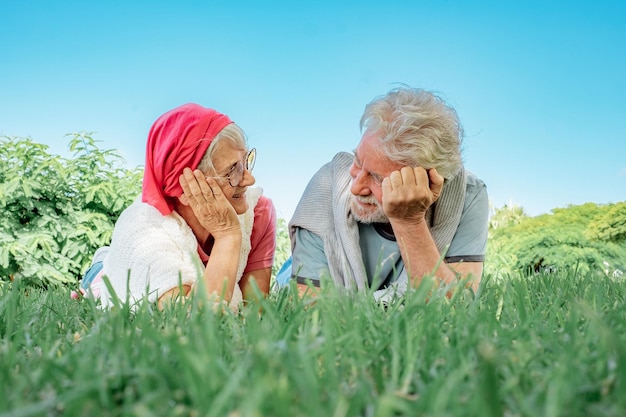 Portret starszej uśmiechniętej pary leżącej na trawie w parku publicznym patrzącej sobie w oczy