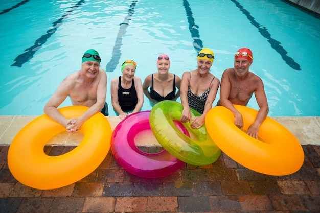 Portret starszych pływaków z nadmuchiwanymi pierścieniami stojącymi przy basenie