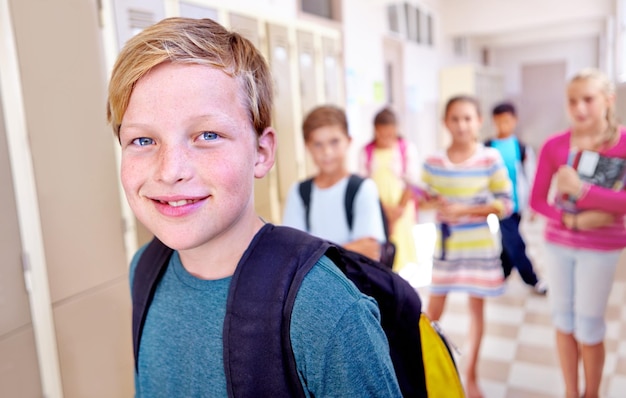 Portret studenta i dziecka z uśmiechem na korytarzu z nauką i plecakiem na powrót do szkoły Młody młody chłopiec i uczenie się z przyjaciółmi na kampusie z dziećmi i szczęśliwy na korytowie