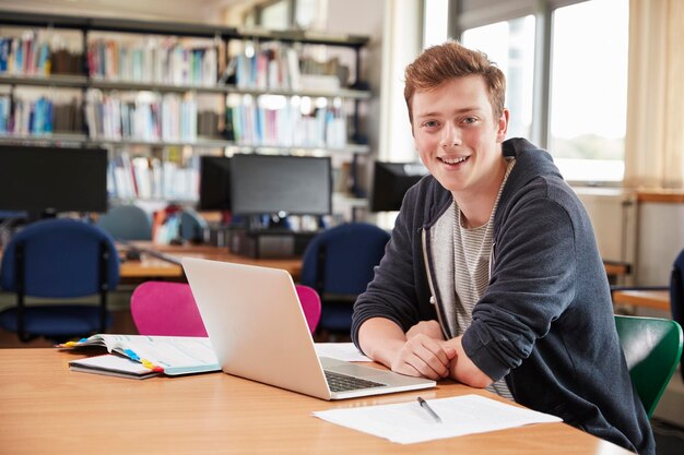 Portret studenta pracującego na laptopie w bibliotece uczelni