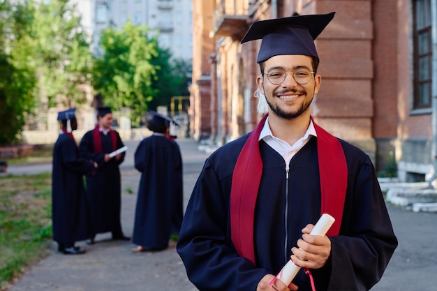 Portret studenta w szlafroku uśmiechającego się do kamery, stojącego na zewnątrz przed uniwersytetem