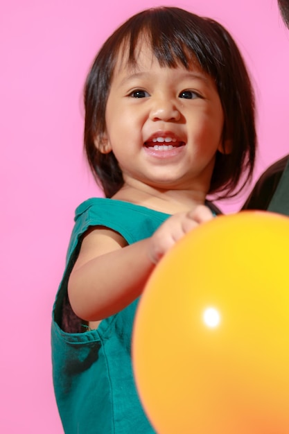 Portret studio strzał mała śliczna azjatycka przedszkolna dziewczynka modelka córka w casualowej długiej sukience trzymająca kolorowe balony na różowym tle