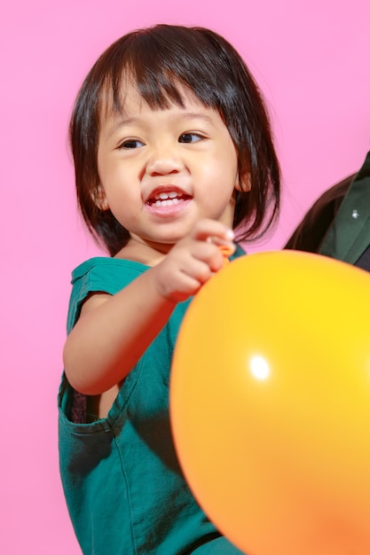 Portret studio strzał mała śliczna azjatycka przedszkolna dziewczynka modelka córka w casualowej długiej sukience trzymająca kolorowe balony na różowym tle