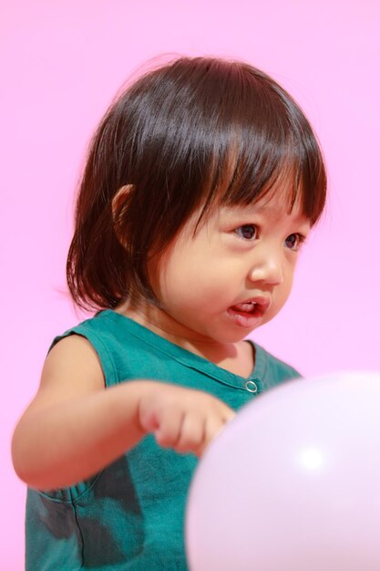 Portret studio strzał mała śliczna azjatycka przedszkolna dziewczynka modelka córka w casualowej długiej sukience trzymająca kolorowe balony na różowym tle