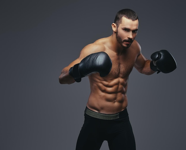 Portret studyjny półnagi brutalny bokser sportowy ubrany w czarne rękawice bokserskie na szarym tle.
