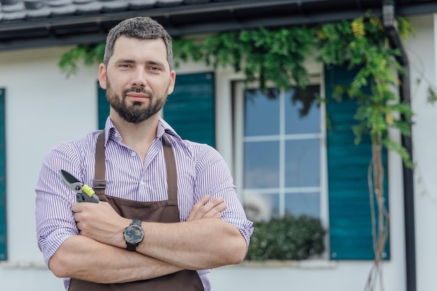 Portret stylowego faceta ogrodnika z nożyczkami ogrodowymi w ogrodzie roślin