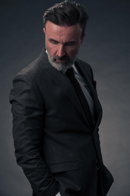 Portret stylowy elegancki starszy biznesmen z brodą i dorywczo ubrania biznesowe w studio fotograficznym na białym tle na ciemnym tle, gestykulując rękami. Zdjęcie wysokiej jakości