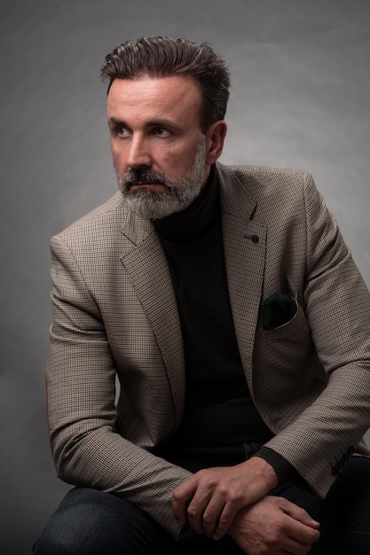 Portret stylowy elegancki starszy biznesmen z brodą i dorywczo ubrania biznesowe w studio fotograficznym na białym tle na ciemnym tle, gestykulując rękami. Zdjęcie wysokiej jakości