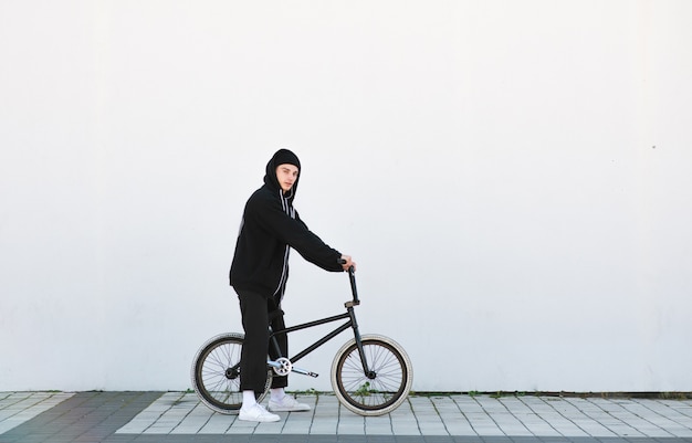 Portret stylowy młody człowiek z rowerem bmx na białej ścianie.