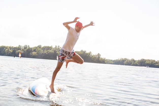 Portret surfera z deską SUP na plaży. Młody człowiek na paddleboard o świcie. Pojęcie sportów ekstremalnych. Styl życia męskiego surfera.