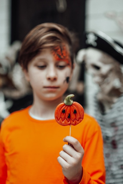 Portret szczerego autentycznego nastoletniego chłopca z pomalowaną twarzą na imprezie Halloween z Jackiem Lollipopem