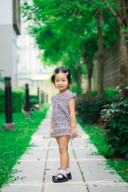 Portret szczęśliwa azjatykcia mała dziewczynka w smokingowej pozyci na footpath w parku