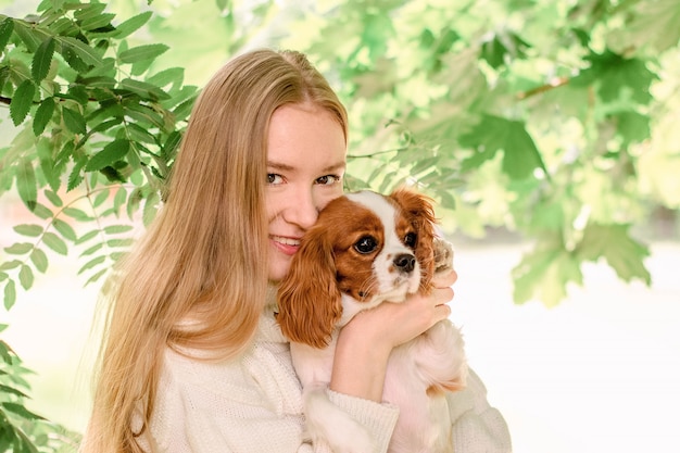 Portret Szczęśliwa Blondynka Z Długimi Włosami, Trzymając śliczny Rasowy Szczeniak Cavalier King Charles Spaniel.