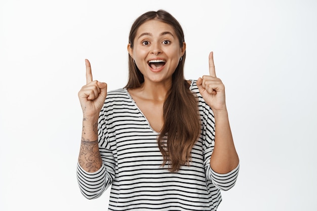 Portret szczęśliwa entuzjastyczna kobieta pokazuje transparent sprzedaży, wskazując palcami na logo i uśmiechając się podekscytowany na białym.