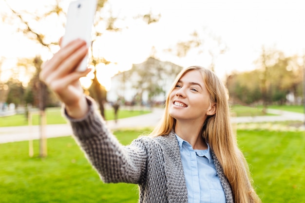 Portret szczęśliwa kobiety pozycja w parku z smartphone.