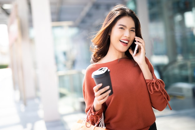Portret szczęśliwa ładna kobieta trzyma filiżankę podczas gdy używać smartphone